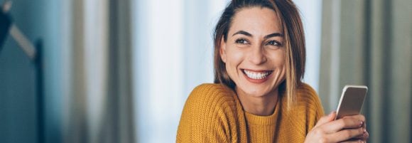 Happy woman sitting with a smartphone over a cup