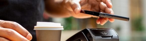 Una mano paga un caffè da asporto con uno smartphone tramite un terminale per carte