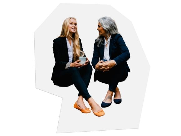 Due donne in outfit da ufficio sedute una accanto all’altra conversano.