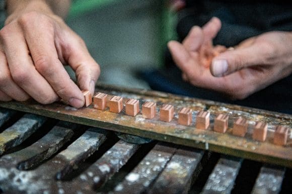La foto in primo piano mostra le mani di un operaio che assembla un pezzo metallico.