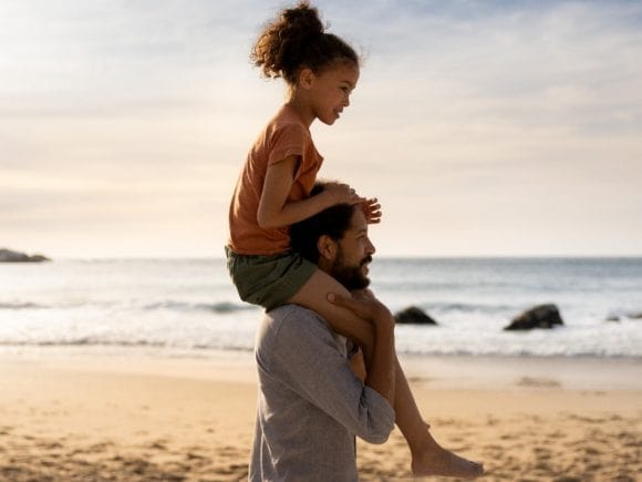Vater trägt Tochter auf seinen Schultern am Strand.