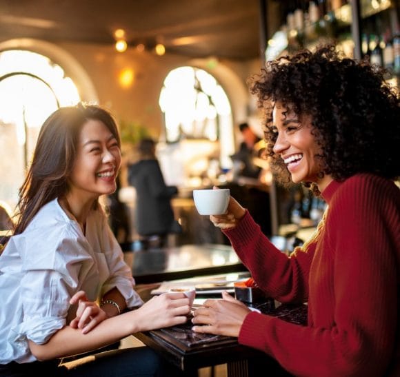 Due donne sorridenti parlano in un bar.