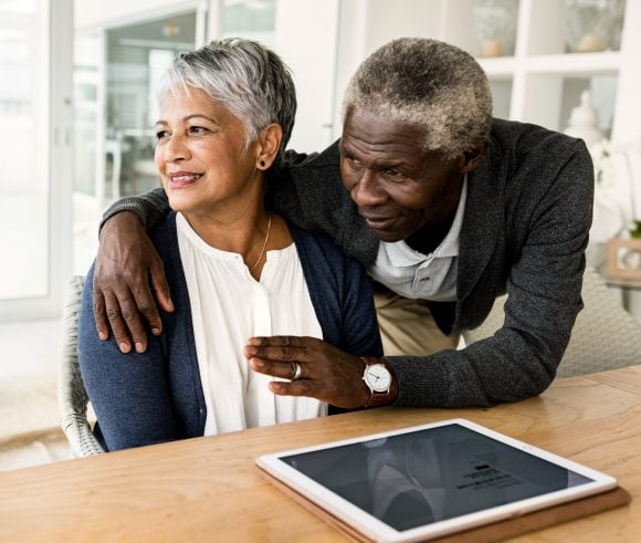 Coppia di anziani seduti a tavola l’una accanto all’altro, sorridono e guardano in lontananza.