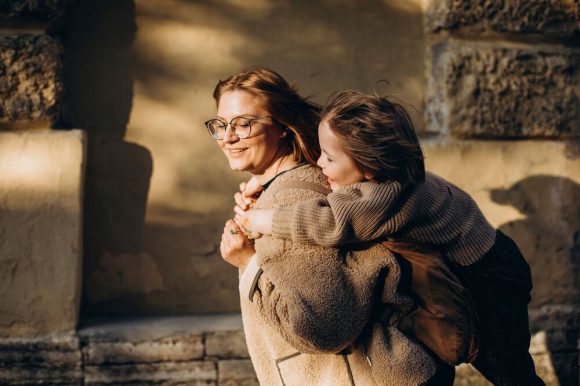Una donna sorridente con gli occhiali porta una bambina sulle spalle