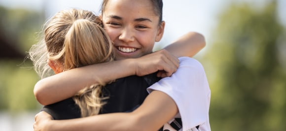 The image shows two girls embracing with joy at the UBS Kids Cup. They are dressed in sportswear and celebrating their achievement.