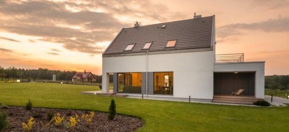 Sur l’image, on voit une maison individuelle sur une prairie verte au coucher du soleil.