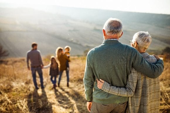 Old couple hanging and seeing the young family with father, mother and children at a sunny field.