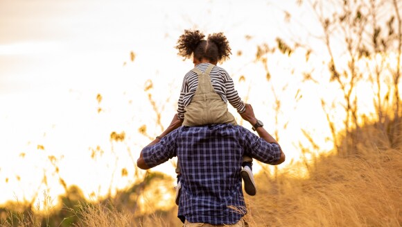 Daughter riding on her father’s shoulders in a meadow