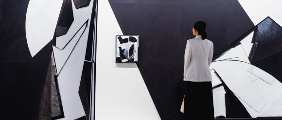 A visitor in a white blazer views a large black-and-white geometric installation.