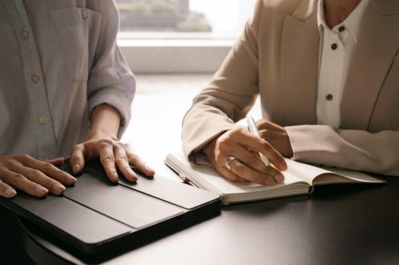 Zwei Menschen in einem Gespräch, ein Tablet und ein Notizbuch in der Hand