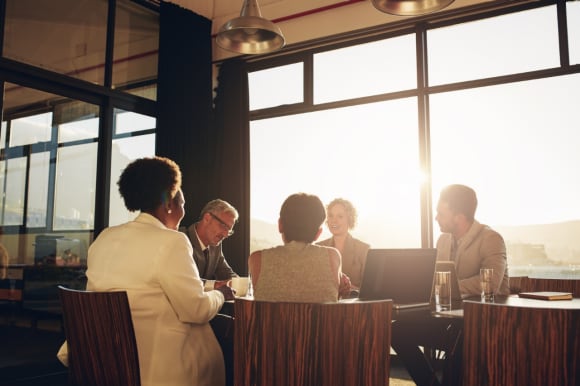 5 personnes assises autour d’une table dans une salle de réunion. Le soleil brille par la fenêtre.