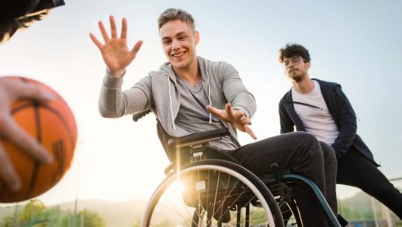 Drei Freunde spielen Basketball, einer davon ist im Rollstuhl