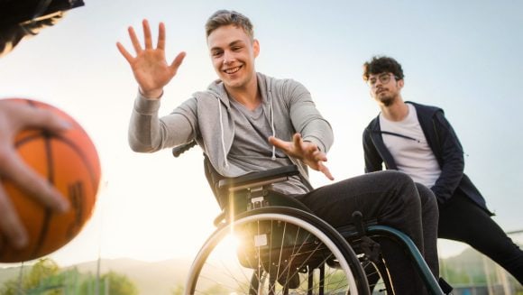 Drei Freunde spielen Basketball, einer davon ist im Rollstuhl