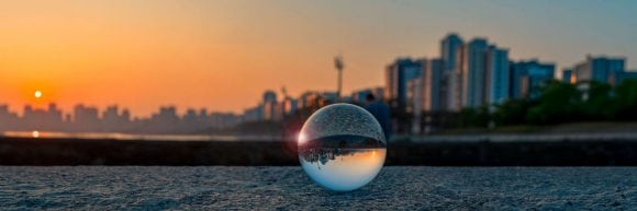 Glass sphere reflecting an upside-down row of colourful buildings on a sunlit street.