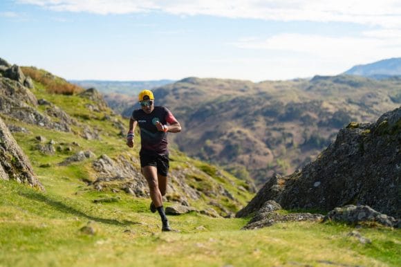 Jeevendra mid-run on a rugged trail in the Lake District, surrounded by misty peaks and dramatic skies