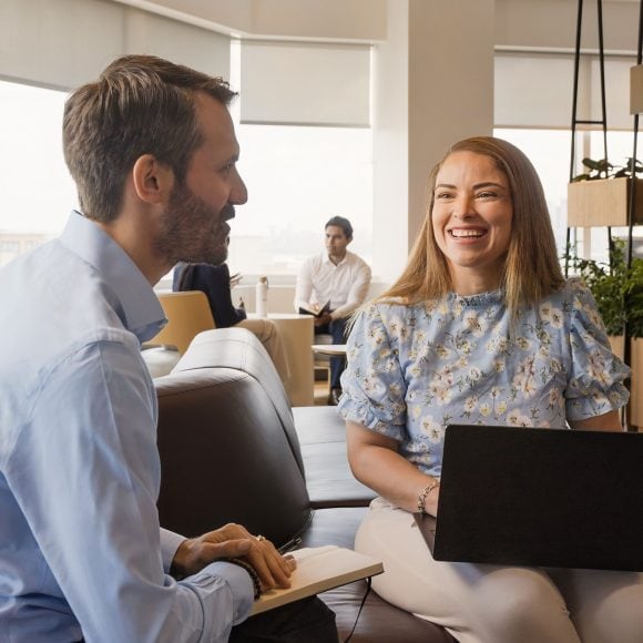 two people in the office talking to each other holding a laptop