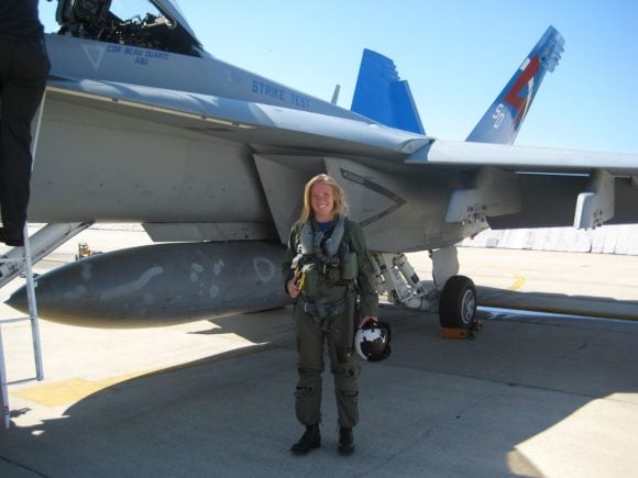 Woman in uniform with flight gear on standing in front of a plane