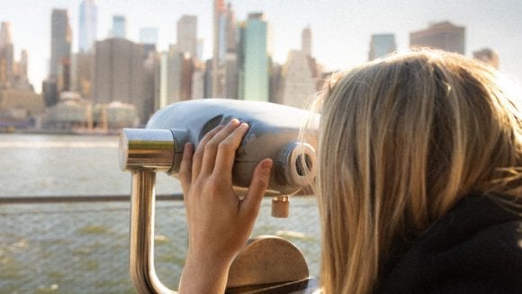 woman looking through binoculars at skyline