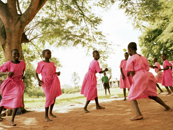 Happy girls in vibrant pink dresses dancing barefoot under a large tree