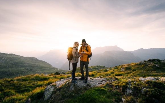 Two hikers on a mountain top looking at a compass at sunset