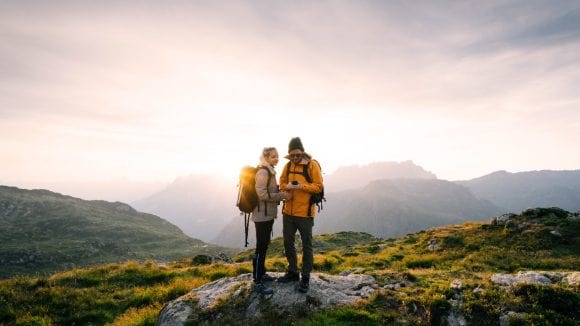 Two hikers on a mountain top looking at a compass at sunset
