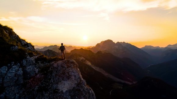 Hiker standing on mountain peak at sunset