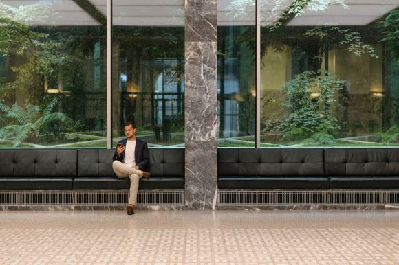 Hombre sentado en un edificio de negocios mirando su celular móvil