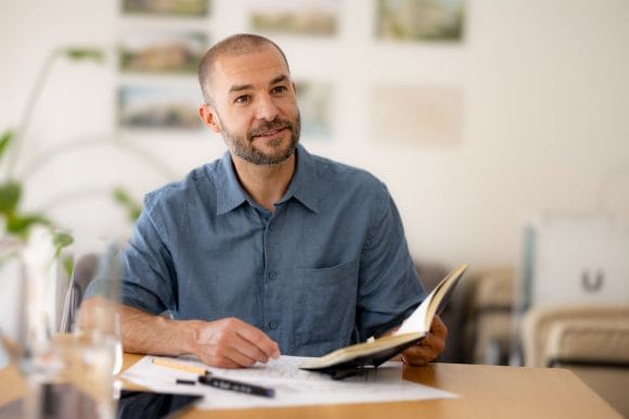 Hombre sentado revisando documentos y sosteniendo una libreta en una oficina.