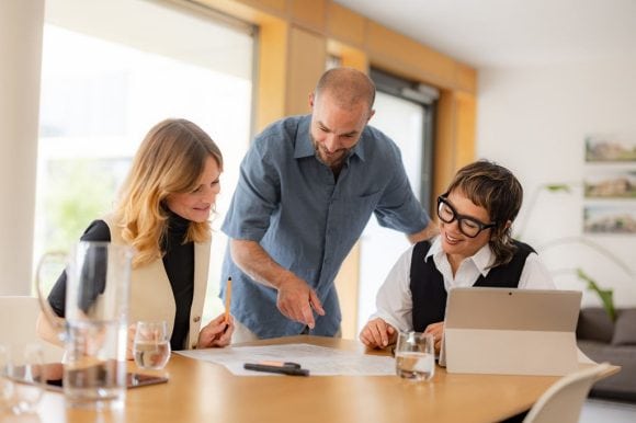 Equipo de trabajo revisando documentos y colaborando en una mesa con computadora portátil.