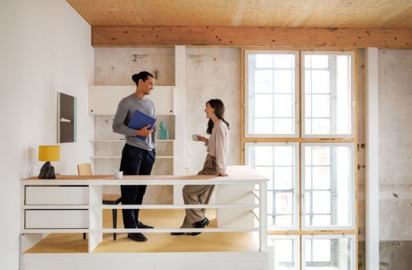 Dos personas sonríen mientras trabajan con una computadora portátil en un espacio interior.