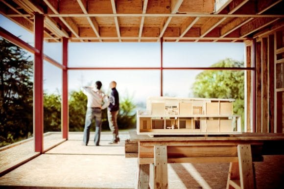 Dos personas observan el paisaje desde una estructura en construcción con maqueta arquitectónica.