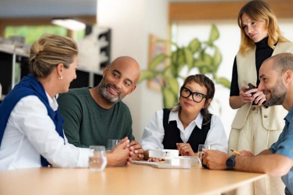 Equipo de trabajo sonríe y conversa durante una reunión en entorno de oficina.