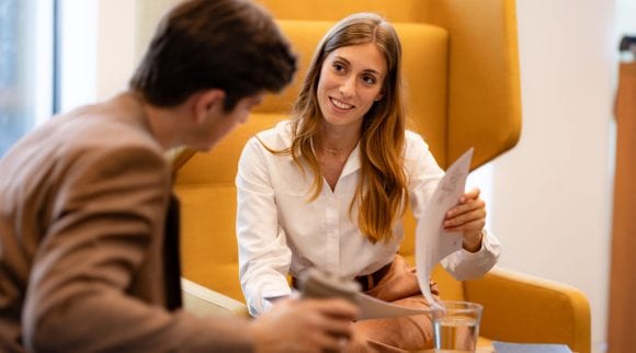 Mujer muestra un documento a colega durante una conversación en oficina.