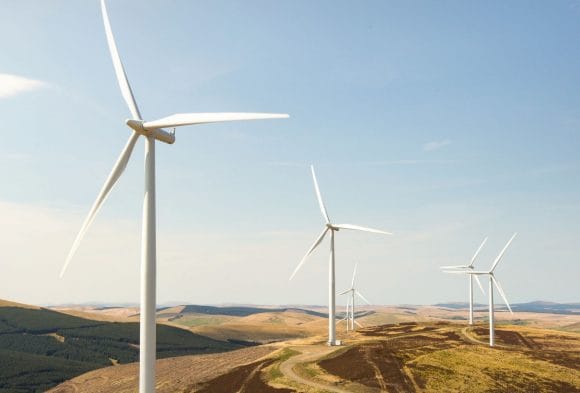 Parque eólico al atardecer con aerogeneradores en un paisaje montañoso.