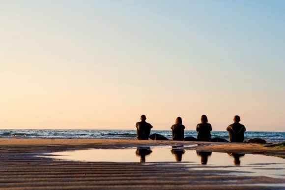 Personas sentadas frente al mar al atardecer.