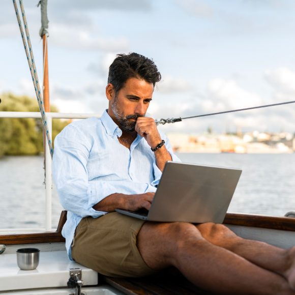 Hombre sentado en un velero trabajando en una computadora portátil