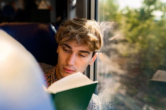 Jeune homme lisant un livre dans le train