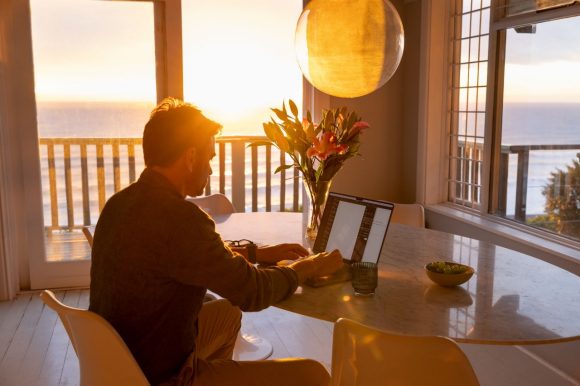 Homem trabalhando no laptop com vista para o mar