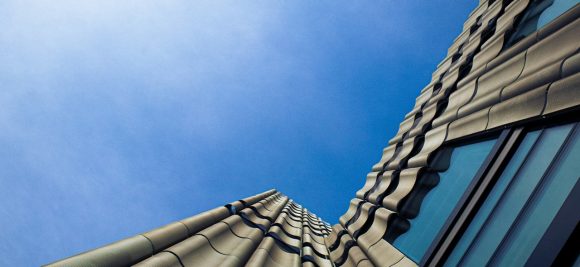 Vista de baixo de prédio alto com fachada ondulada e céu azul.
