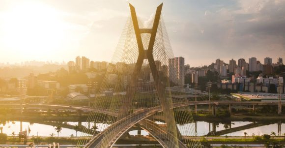 Ponte estaiada sobre rio com skyline urbano ao pôr do sol