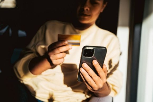 Pessoa com cartão de crédito fazendo uma compra pelo celular