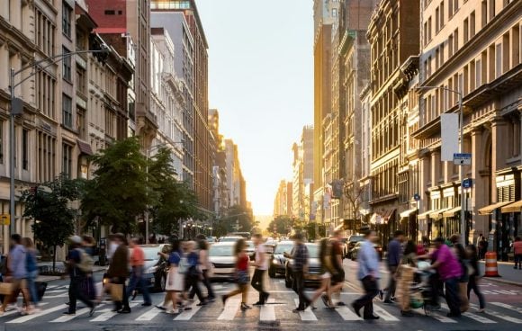 Rua urbana com pedestres atravessando faixa de pedestres ao pôr do sol