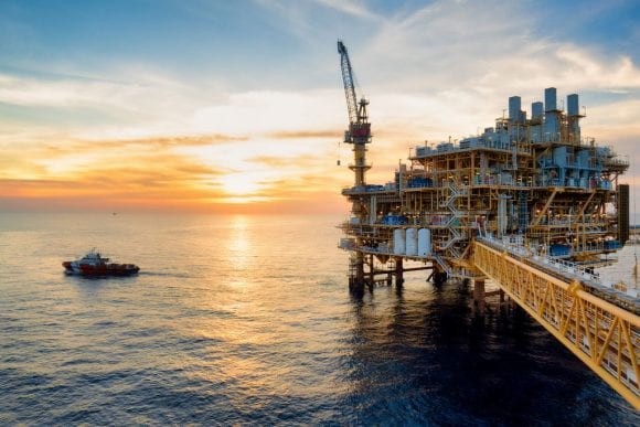 Plataforma de petróleo offshore ao pôr do sol com embarcação próxima no mar.
