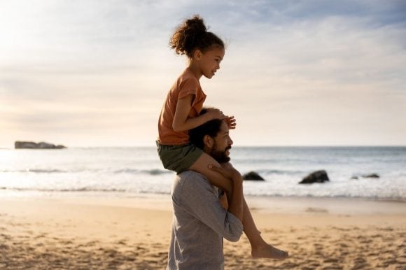 Pai carregando a filha nos ombros na praia ao pôr do sol