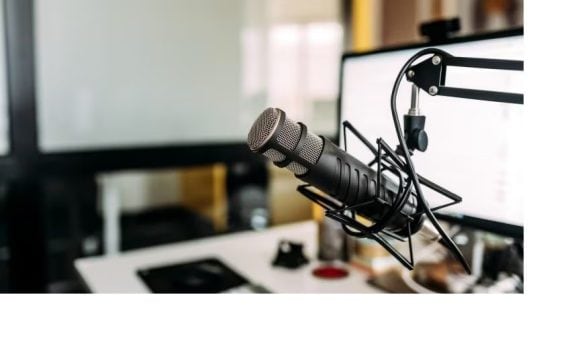 Micrófono de estudio sobre brazo articulado frente a una computadora, fondo desenfocado.