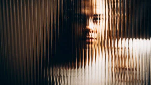 Abstract illustration of a face partially visible through textured glass.