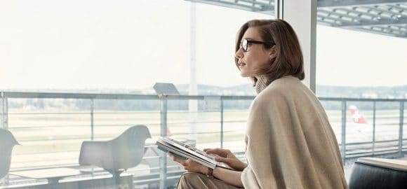 Business woman sitting in a lounge area holding magazines, overlooking the runway. Zurich Airport.