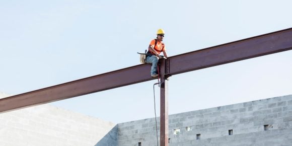 Male builder wearing a visibility vest and helmet sat on top of a building structure