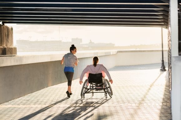 Woman in wheelchair and jogging friend on promenade