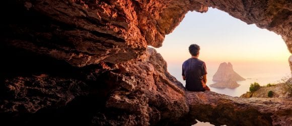 Traveler watching sunset from cave